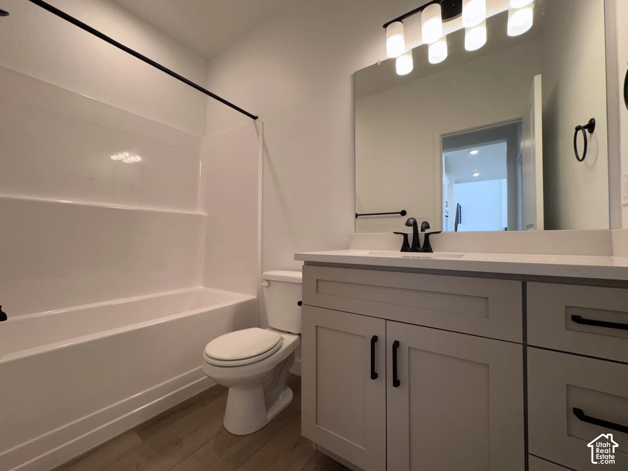Bathroom featuring a white tub/shower combination, wood-finish flooring, a white vanity with shaker-style cabinetry, and a black faucet