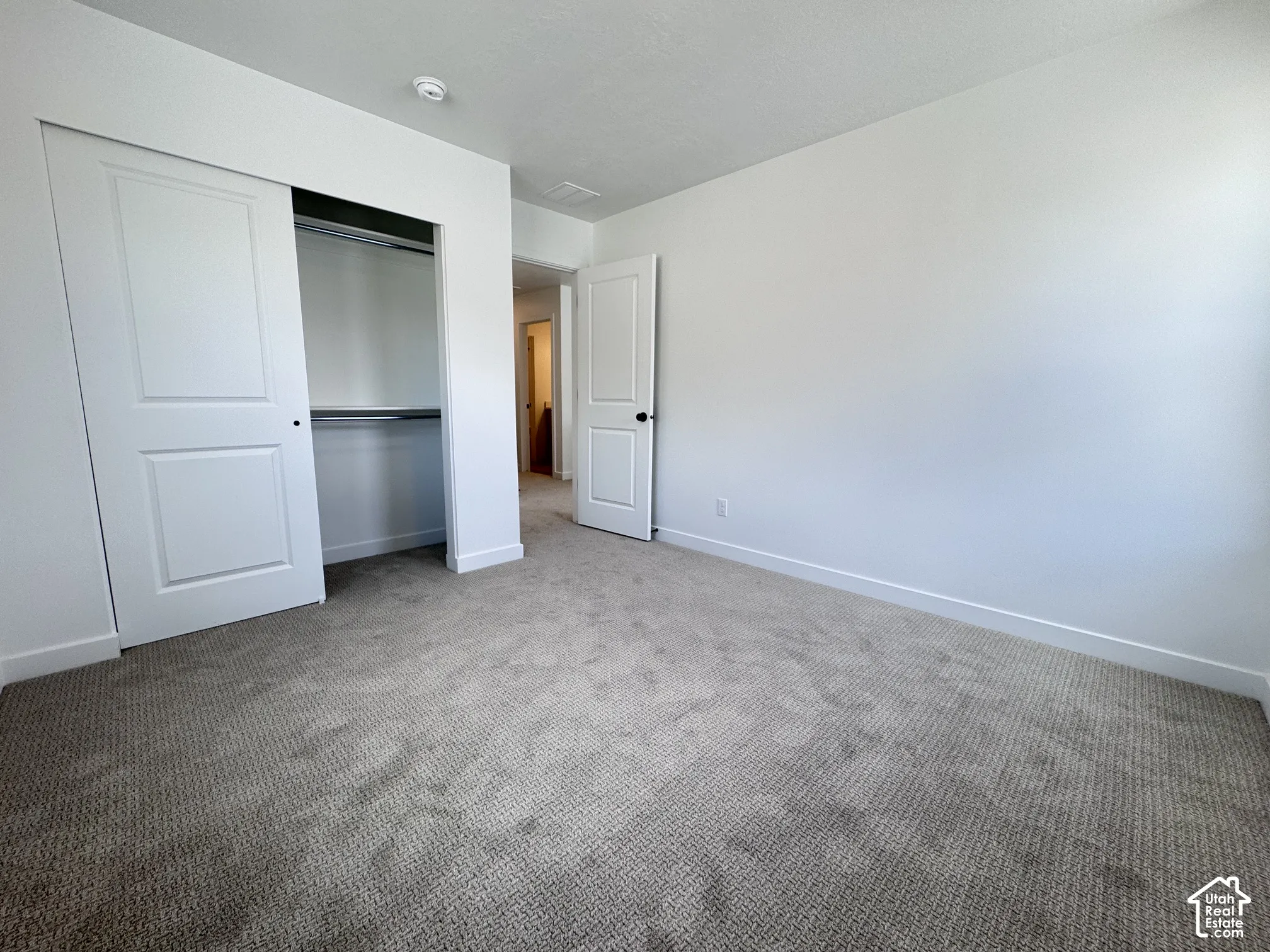 Neutral tone wall paint, textured carpet flooring, white sliding closet doors, and a white interior door with black hardware