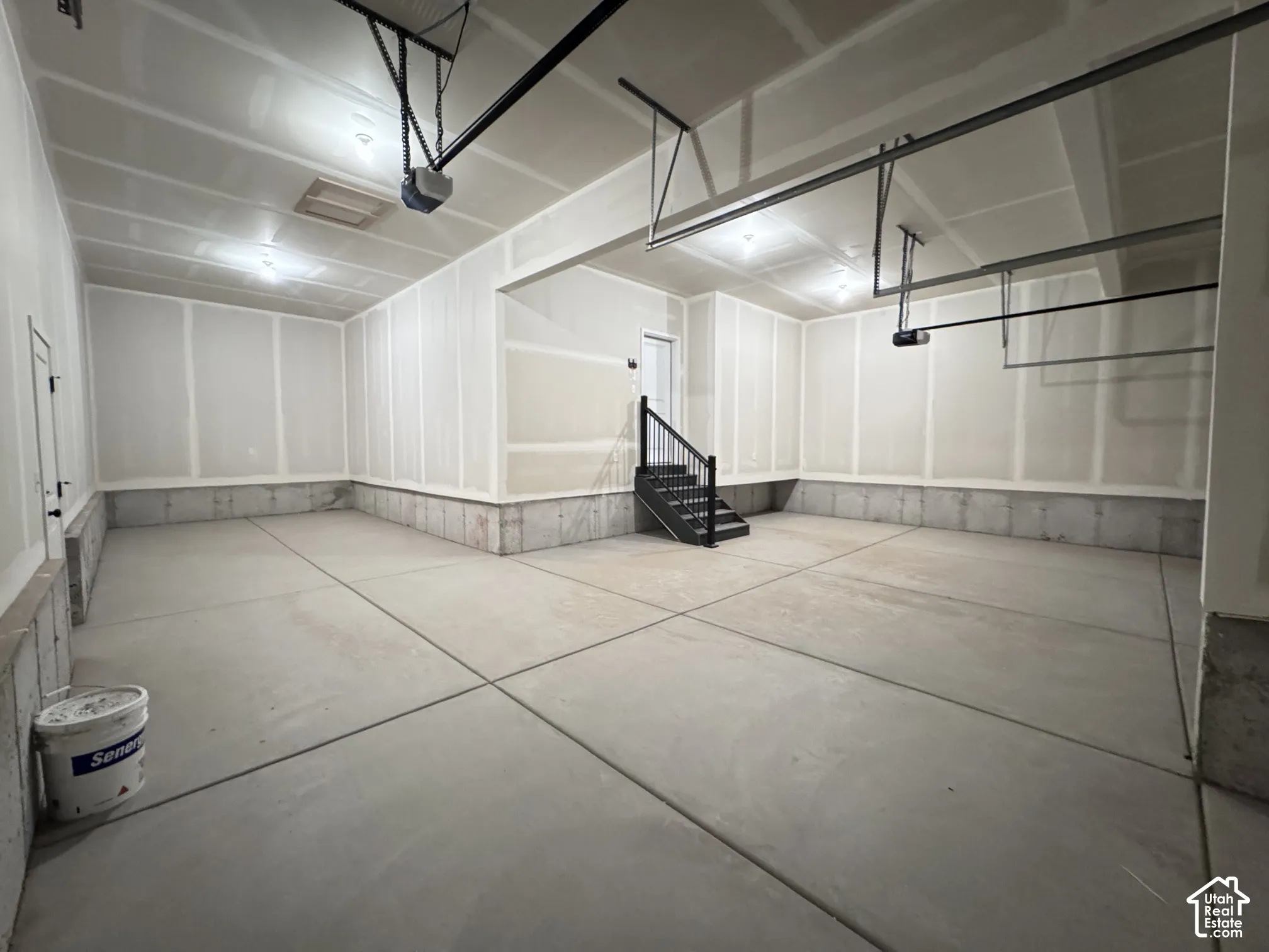 Spacious garage with concrete flooring, exposed ceiling joists, and a built-in staircase with black railing
