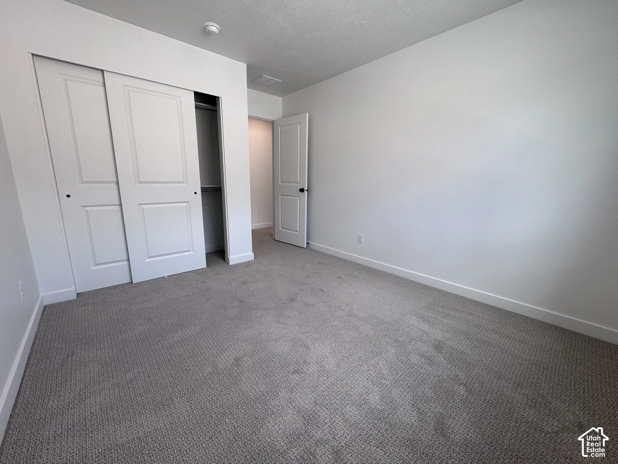 Carpeted flooring, white walls, white sliding closet doors, black door hardware, white interior door
