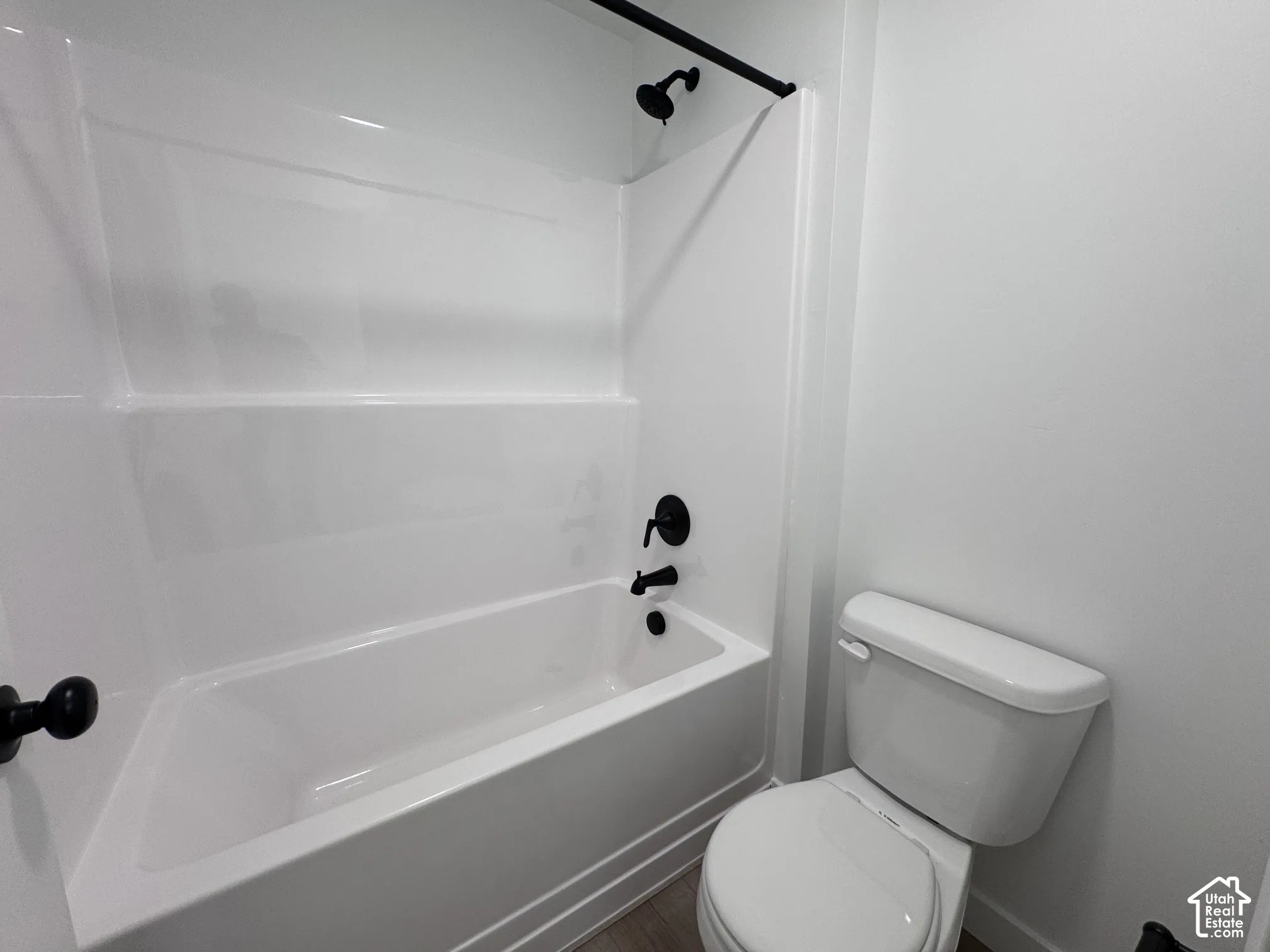 White bathtub with integrated surround and matte black fixtures, alongside a white toilet