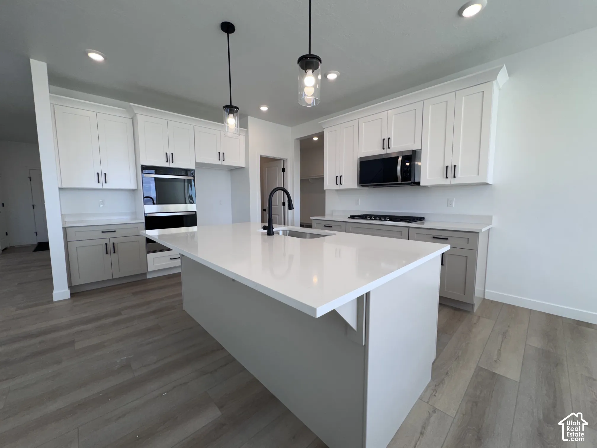 Contemporary kitchen featuring white cabinetry, a large center island with a light-toned countertop, wood-finish flooring, and recessed lighting