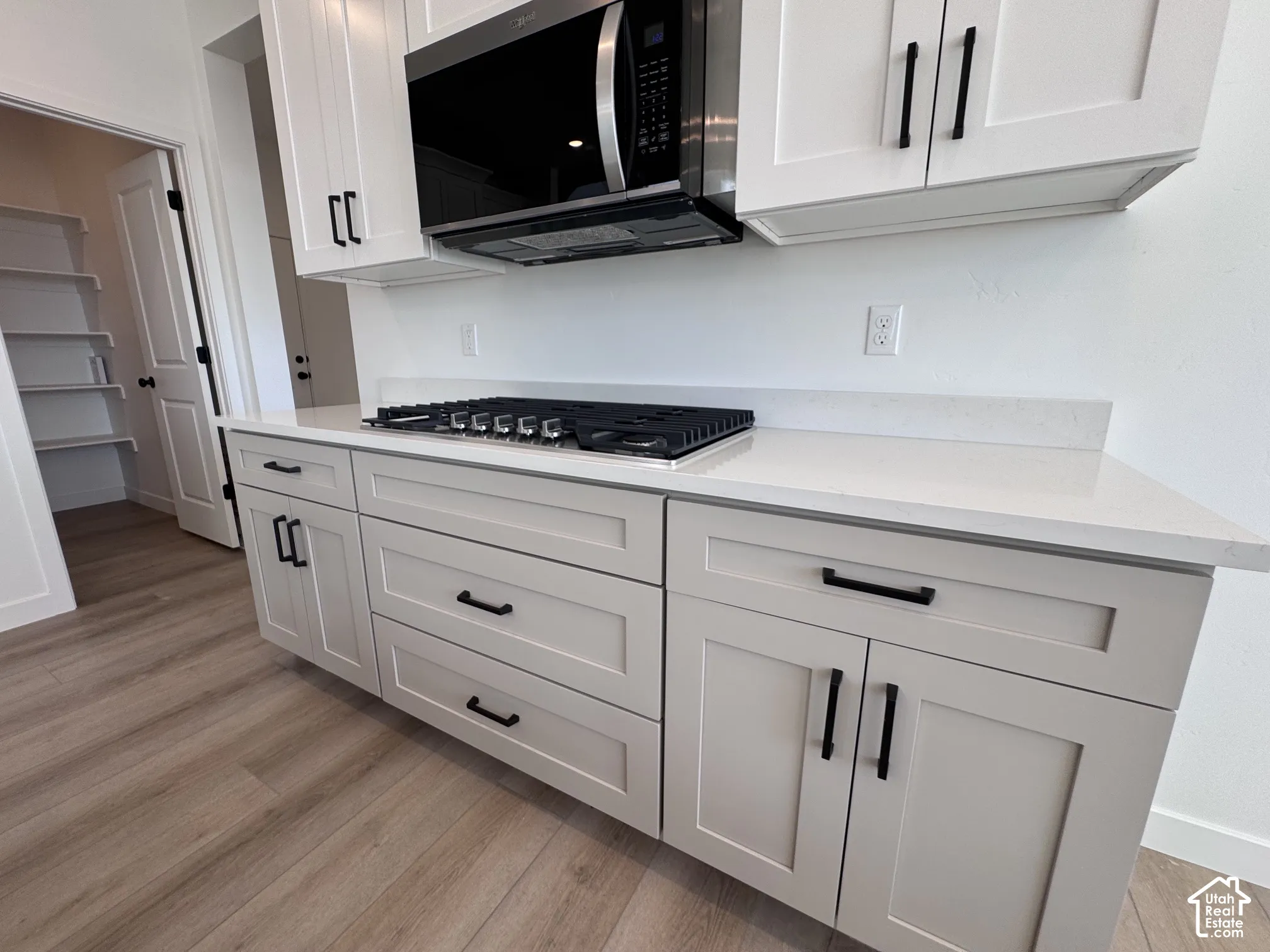 White upper cabinetry with black hardware, integrated microwave, cooktop, and light-toned countertops