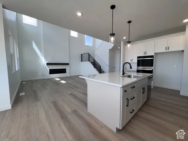 Open-concept living area featuring a kitchen island with sink, integrated double ovens, wood-finish flooring, and a fireplace with a wood-beam mantel