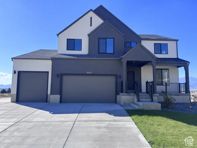 Multi-level exterior featuring a combination of light-toned stucco and dark vertical siding, an attached three-car garage, and a covered front porch with black metal railings