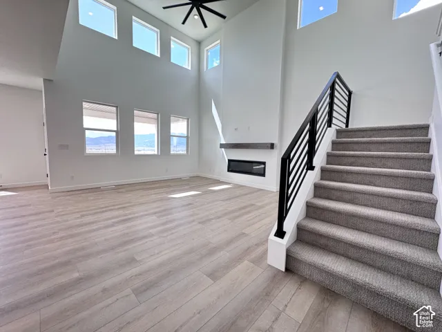 Two-story living area with high ceilings, multiple windows, wood-finish flooring, and a modern fireplace with a mantel