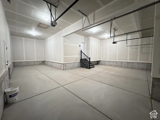 Spacious garage with concrete flooring, exposed ceiling joists, and a built-in staircase with black railing
