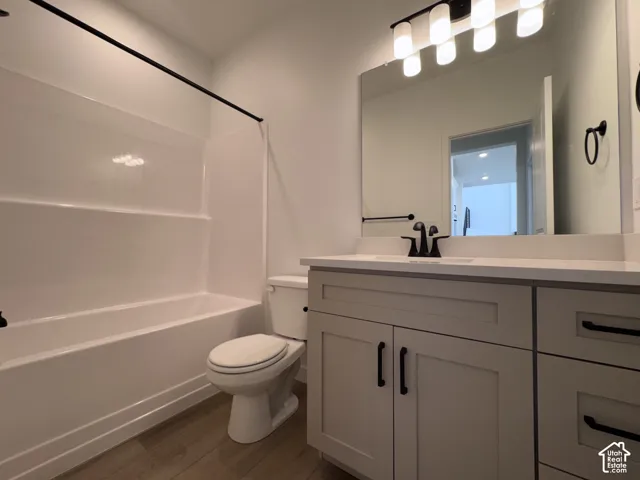 Bathroom featuring a white tub/shower combination, wood-finish flooring, a white vanity with shaker-style cabinetry, and a black faucet