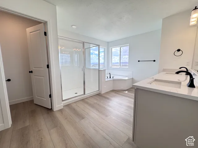 Dual vanity with integrated sinks and black fixtures, corner soaking tub, glass-enclosed shower, and wood-finish flooring