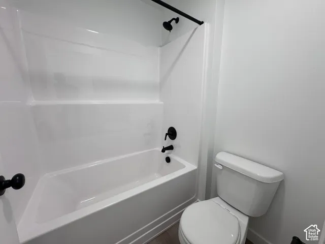 White bathtub with integrated surround and matte black fixtures, alongside a white toilet