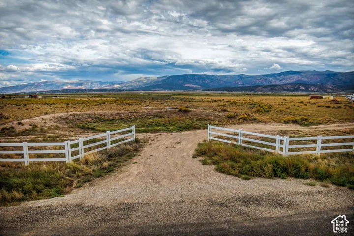 Expansive open land with a white three-rail fence and gravel entry