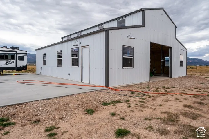 White corrugated metal siding, dark trim, multiple windows, large garage door opening, and concrete pad