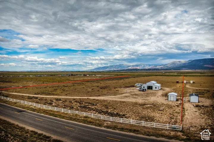 Expansive land parcel featuring a main structure, multiple detached sheds, and a white fence along the roadside