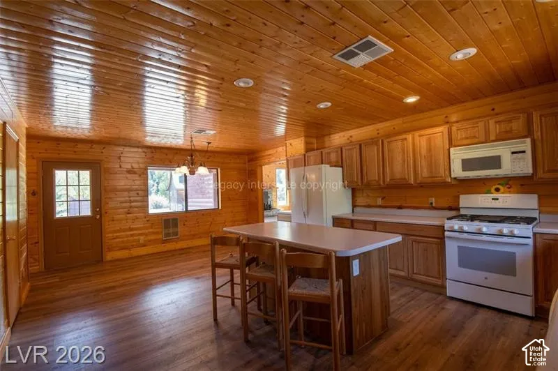 Wood-finish flooring, wood plank walls, wood plank ceiling with recessed lighting, kitchen island with built-in storage, and full range with microwave