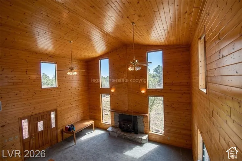 Vaulted wood-paneled ceilings, wood-paneled walls, stone fireplace with hearth, multiple windows, and a wood entry door with glass inserts