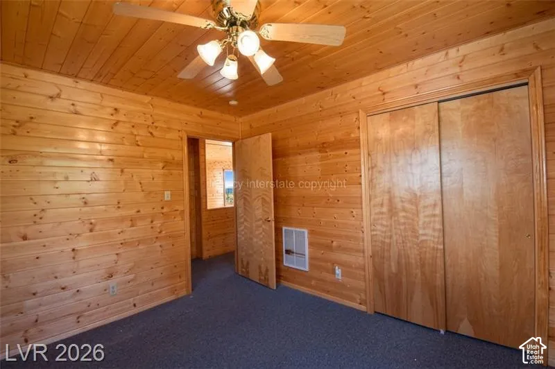 Wood-paneled walls and ceiling, ceiling fan with integrated lighting, built-in sliding closet, and dark carpet flooring