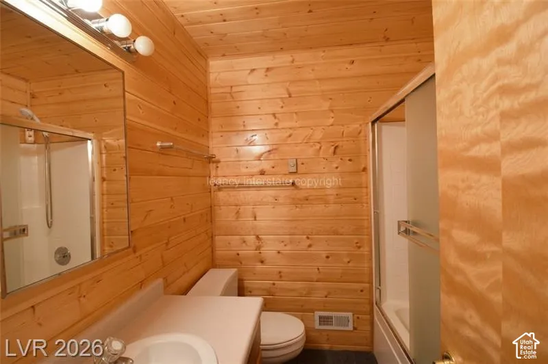 Wood-paneled walls, vanity with integrated sink, wall-mounted mirror, three-bulb vanity light fixture, and enclosed shower with sliding glass door