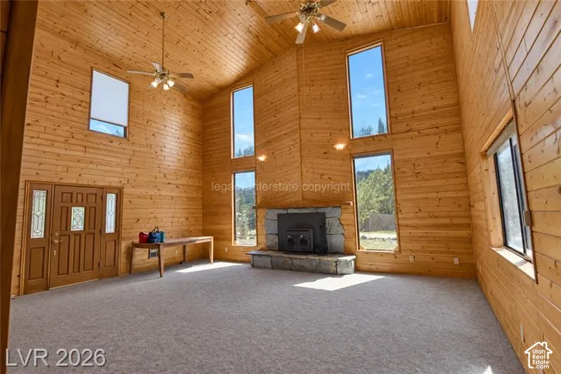 Vaulted wood-paneled ceilings, stone-faced fireplace with hearth, multiple large windows, ceiling fans, and a double entry door with sidelights
