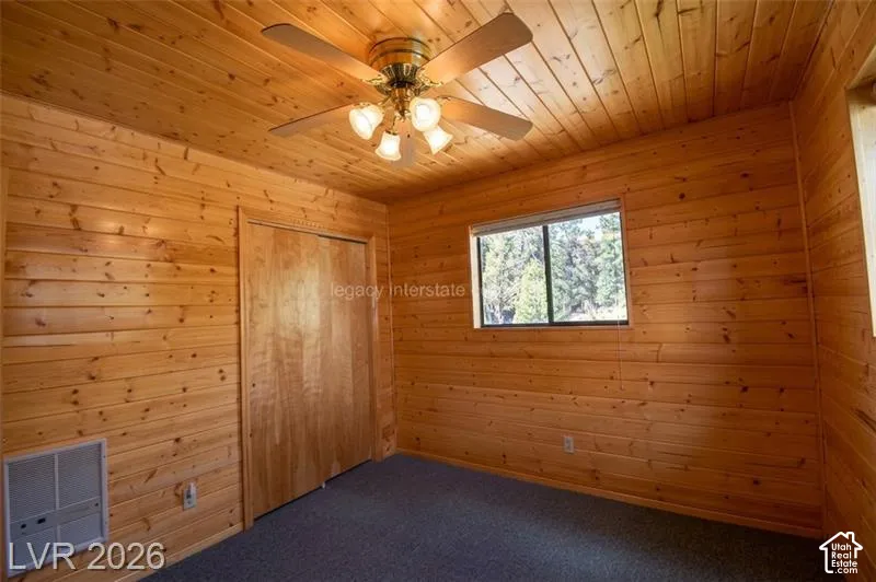 Wood-paneled walls and ceiling, ceiling fan with integrated lighting, window with exterior scenery, wood-finish closet doors, and carpet flooring