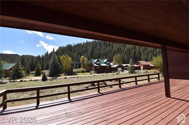 Expansive wood-finish deck with a rustic railing, offering open-air seating and a backdrop of dense evergreen trees