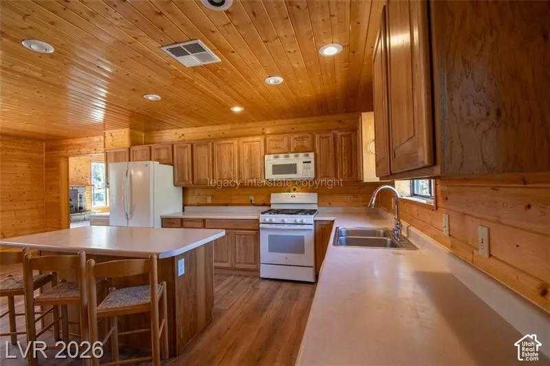 Wood-paneled walls and ceiling, recessed lighting, wood-finish flooring, kitchen island with seating, double basin stainless steel sink