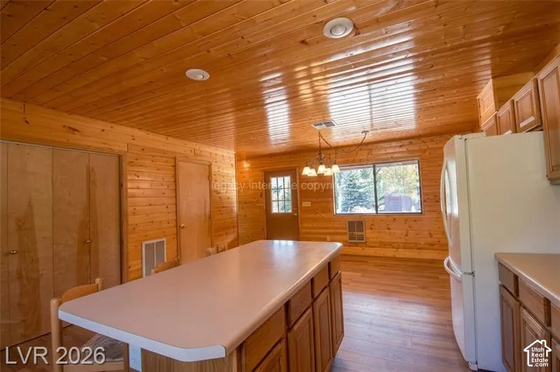 Wood-paneled walls and ceiling, recessed lighting, central kitchen island with light-colored countertop, wood-finish flooring, and built-in cabinetry
