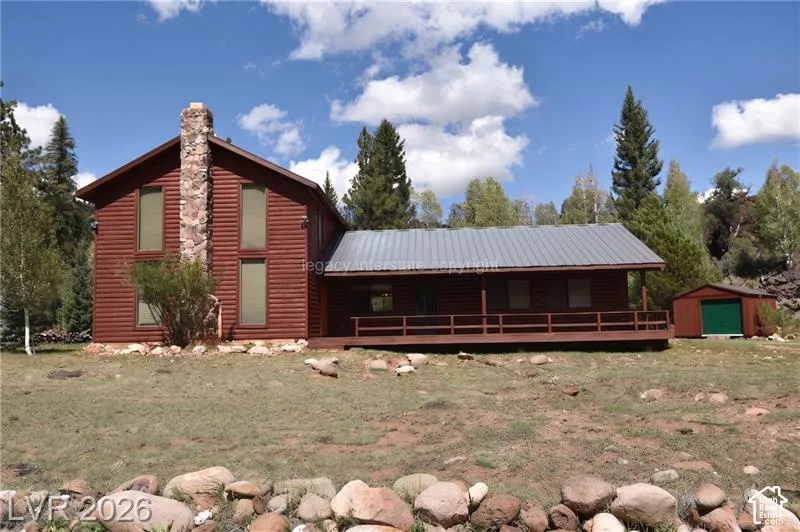 Red wood-sided exterior with a stone chimney, a covered porch, a metal roof, and a detached shed