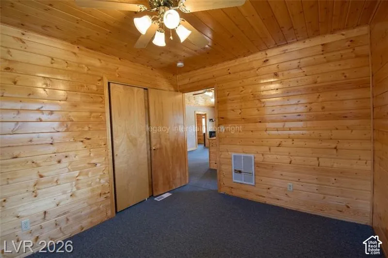 Wood-paneled walls and ceiling, ceiling fan with integrated lighting, two light-toned wood doors, and dark carpet flooring