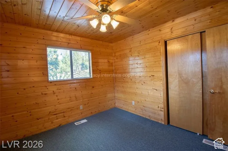 Wood-paneled walls and ceiling, wall-to-wall carpeting, window with outdoor scenery, and a ceiling fan with integrated lighting
