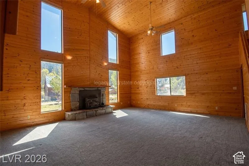 Expansive room with high vaulted wood-paneled ceilings, a stone-clad fireplace with a hearth, and multiple windows