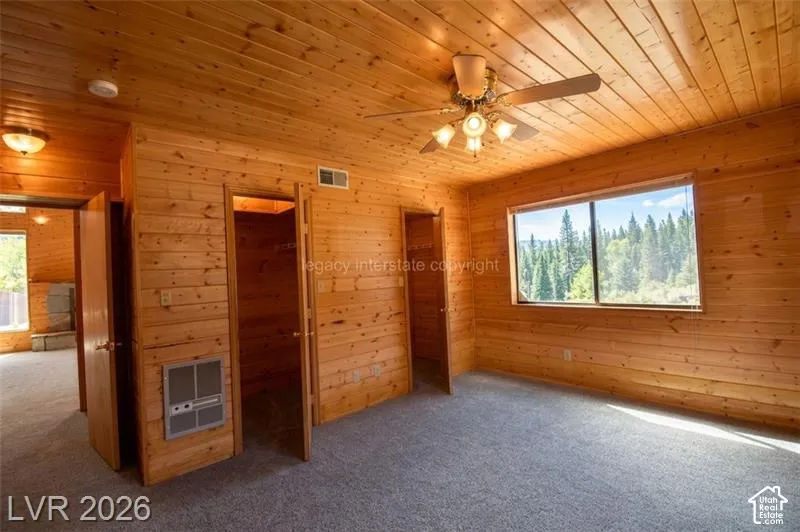 Wood-paneled walls and ceiling, wall-to-wall carpeting, ceiling fan with integrated lighting, and a large window showcasing tree scenery