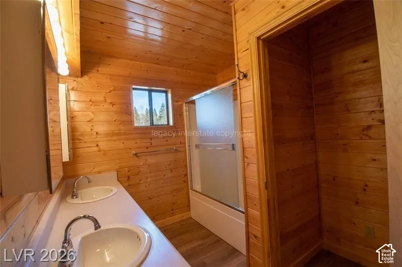 Wood-paneled interior featuring a double vanity with integrated sinks, a built-in shower with a frosted glass enclosure, and a window