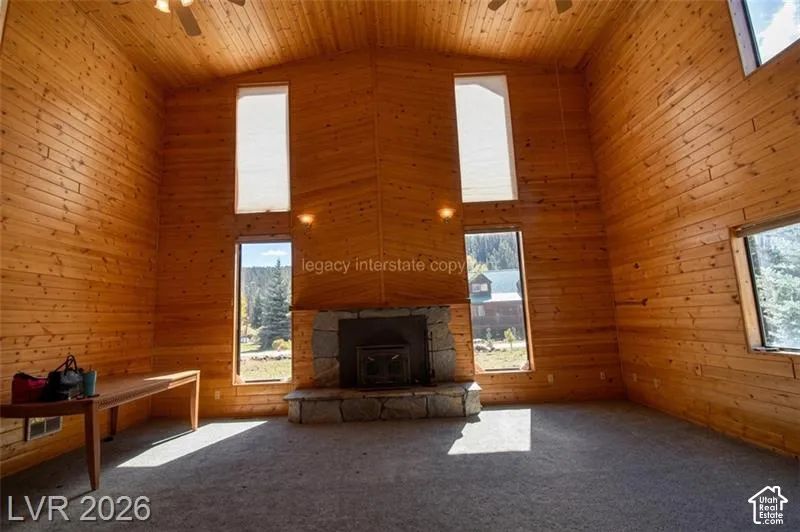 Vaulted ceiling with wood paneling, multiple windows, stone fireplace, and ceiling fan