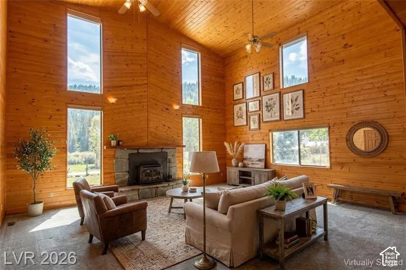 Vaulted wood-paneled ceilings, stone-clad fireplace with wood-burning insert, multiple large windows, natural wood wall finishes, and ceiling fan with integrated lighting