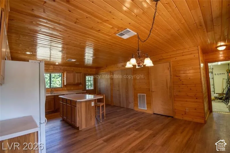 Wood-paneled walls and ceiling, wood-finish flooring, kitchen island with countertop, and cabinet storage