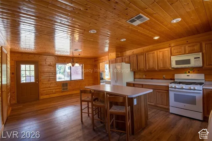 Wood-finish flooring, wood plank walls, wood plank ceiling with recessed lighting, kitchen island with built-in storage, and full range with microwave