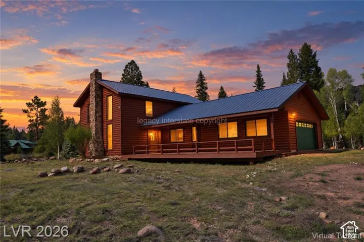Log-style exterior featuring a stone chimney, metal roof, and an expansive deck
