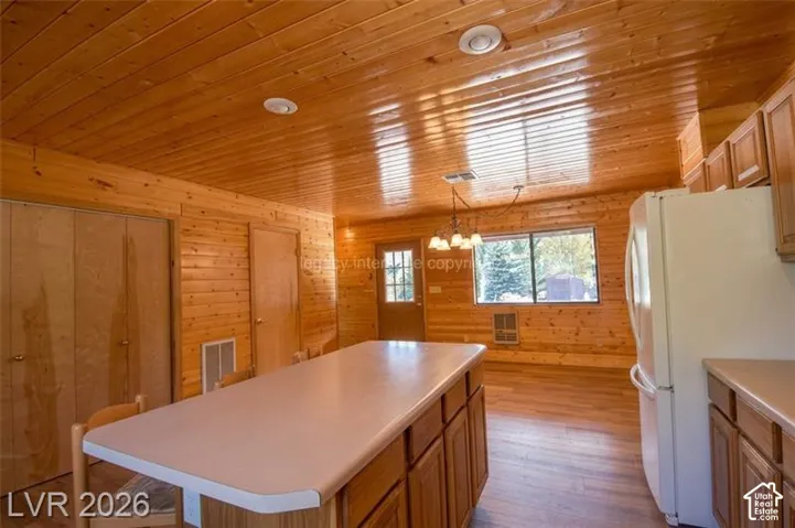 Wood-paneled walls and ceiling, recessed lighting, central kitchen island with light-colored countertop, wood-finish flooring, and built-in cabinetry