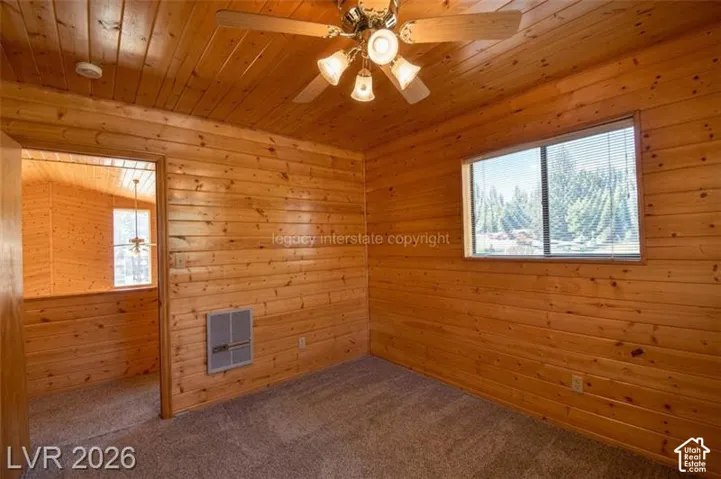 Wood-paneled walls and ceiling, wall-to-wall carpeting, and a ceiling fan with integrated lighting