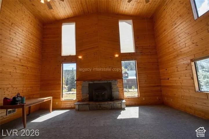 Vaulted ceiling with wood paneling, multiple windows, stone fireplace, and ceiling fan