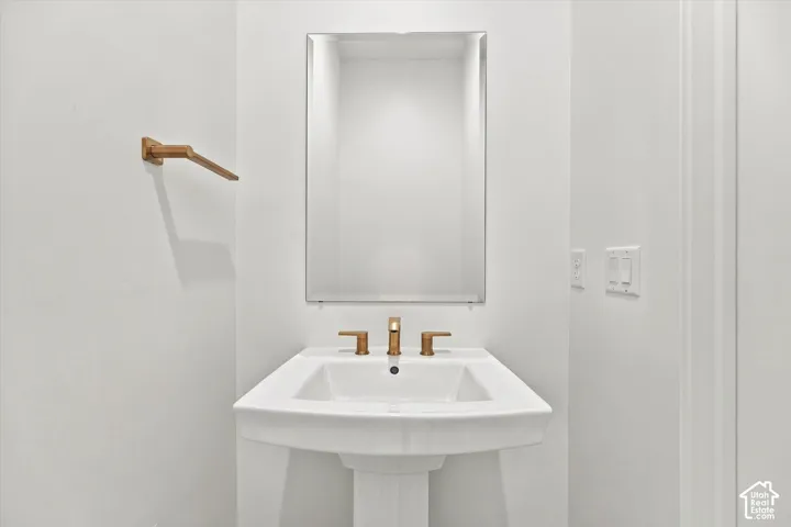 Pedestal sink with a rectangular basin, polished brass-finish faucet, and a wall-mounted mirror with a beveled edge