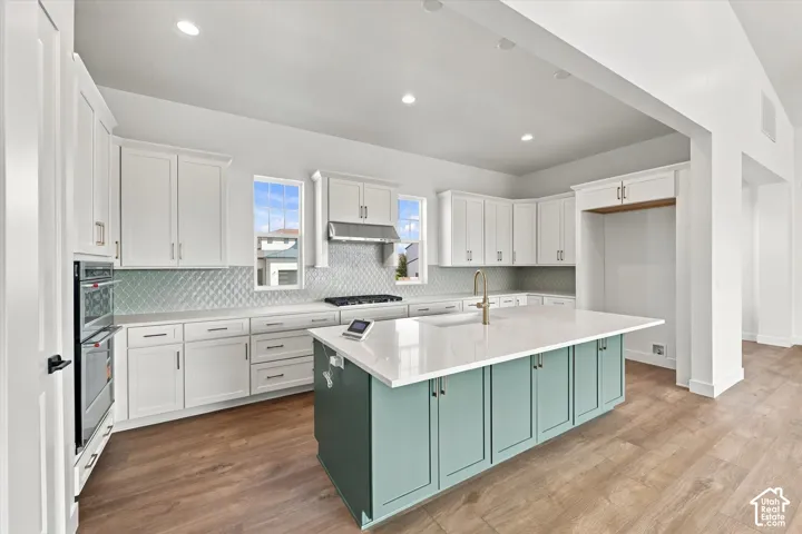 Kitchen featuring a large island with a quartz countertop, white cabinetry, integrated double ovens, and wood-finish flooring