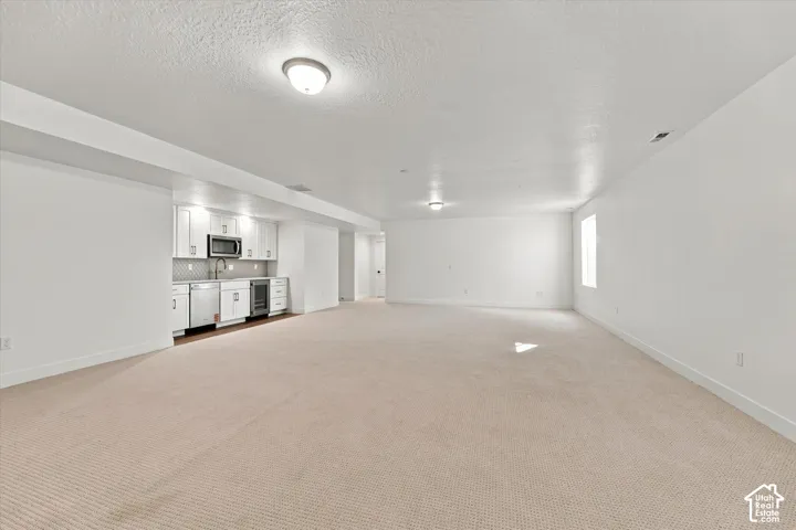 Spacious room featuring neutral carpeting, recessed lighting, and a built-in wet bar with white cabinetry, stainless steel appliances, and a tiled backsplash