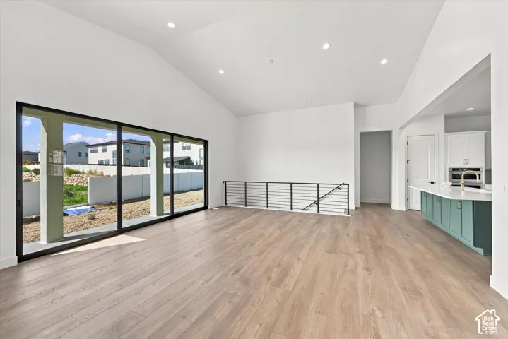 Expansive open-concept living area featuring wood-finish flooring, vaulted ceilings, recessed lighting, and a multi-panel sliding glass door