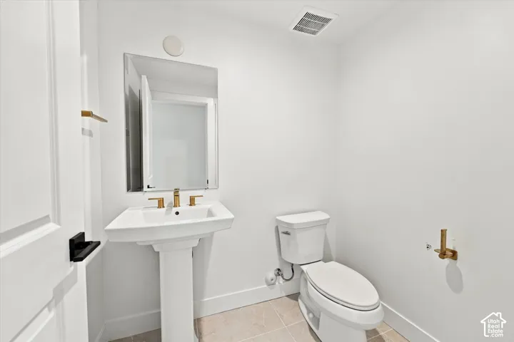 Pedestal sink with gold-finish faucet, rectangular mirror, and white toilet