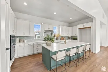 Kitchen featuring a center island with quartz countertops, custom shaker-style cabinetry, stainless steel double wall ovens, a chevron-patterned tile backsplash, and wood-finish flooring