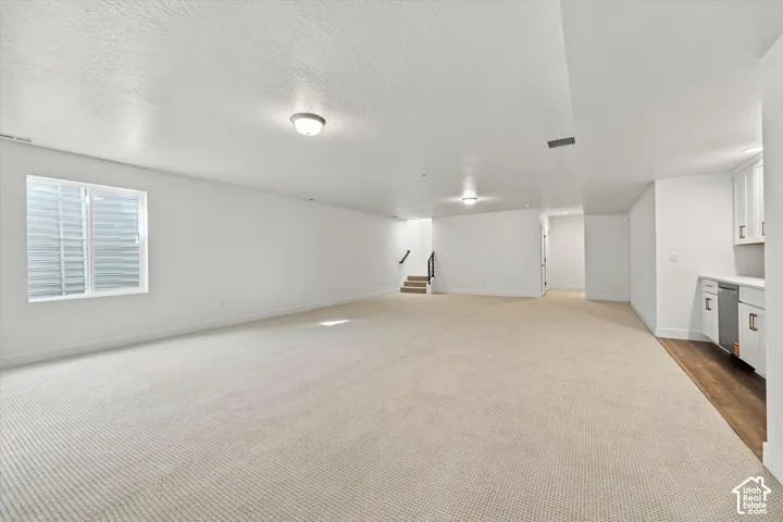 Expansive finished lower level featuring a wet bar with white cabinetry, built-in beverage refrigerator, and solid surface countertop