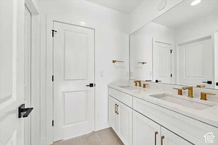 Dual vanity with integrated sinks, gold-finish fixtures, a large wall-mounted mirror, and white shaker-style cabinetry