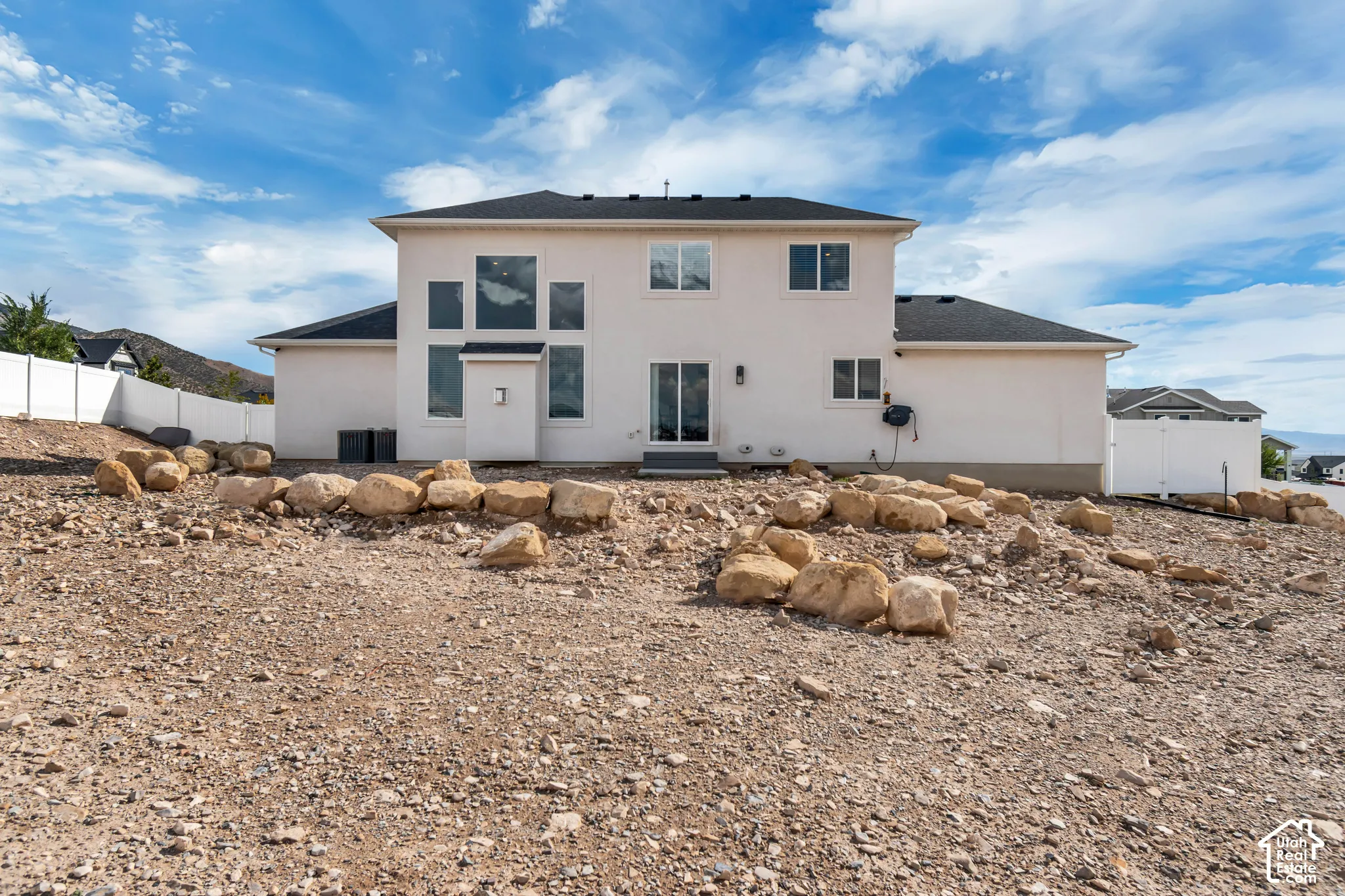 Rear elevation featuring a stucco exterior, dark roof, white vinyl fencing, and a combination of fixed and operable windows