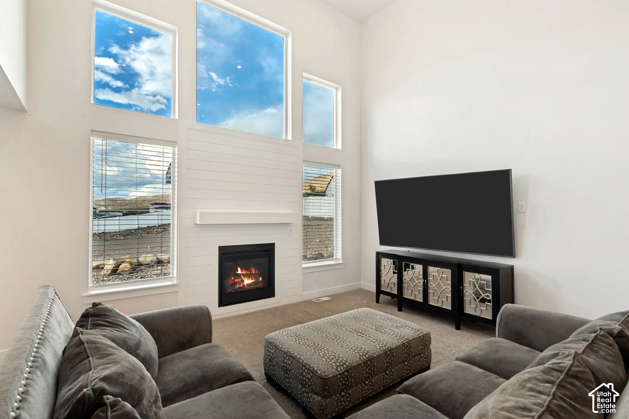 Two-story ceiling with high windows, shiplap-accented fireplace with mantel, built-in fireplace, and carpeted flooring